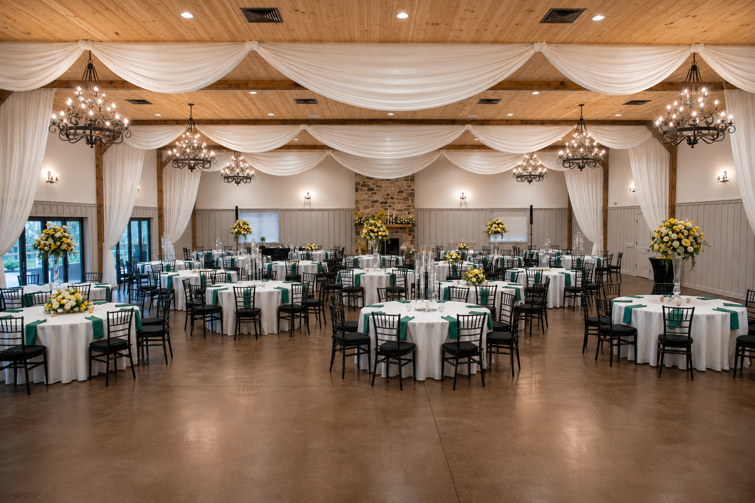 Banquet hall set for a catered event with round tables, chandeliers, and draped ceiling fabric