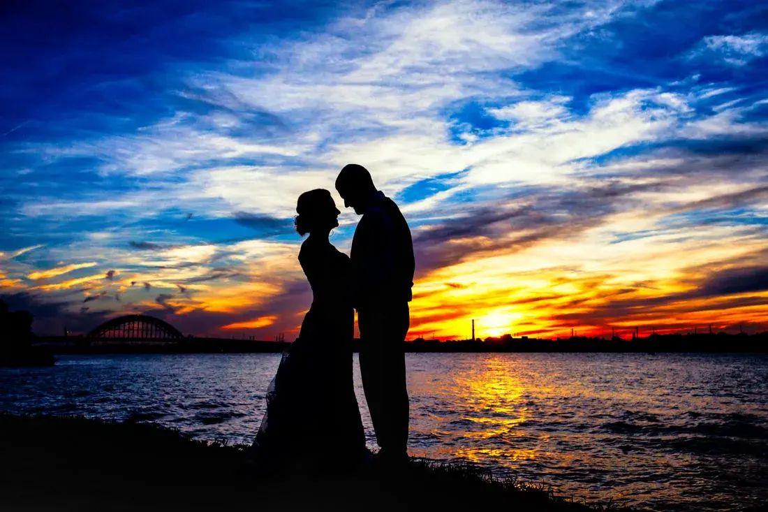 A couple silhouetted against a vivid sunset over the water