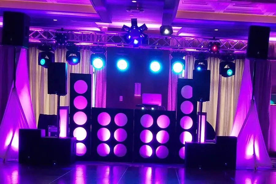 A DJ booth with speakers and truss-mounted lights glowing purple and blue