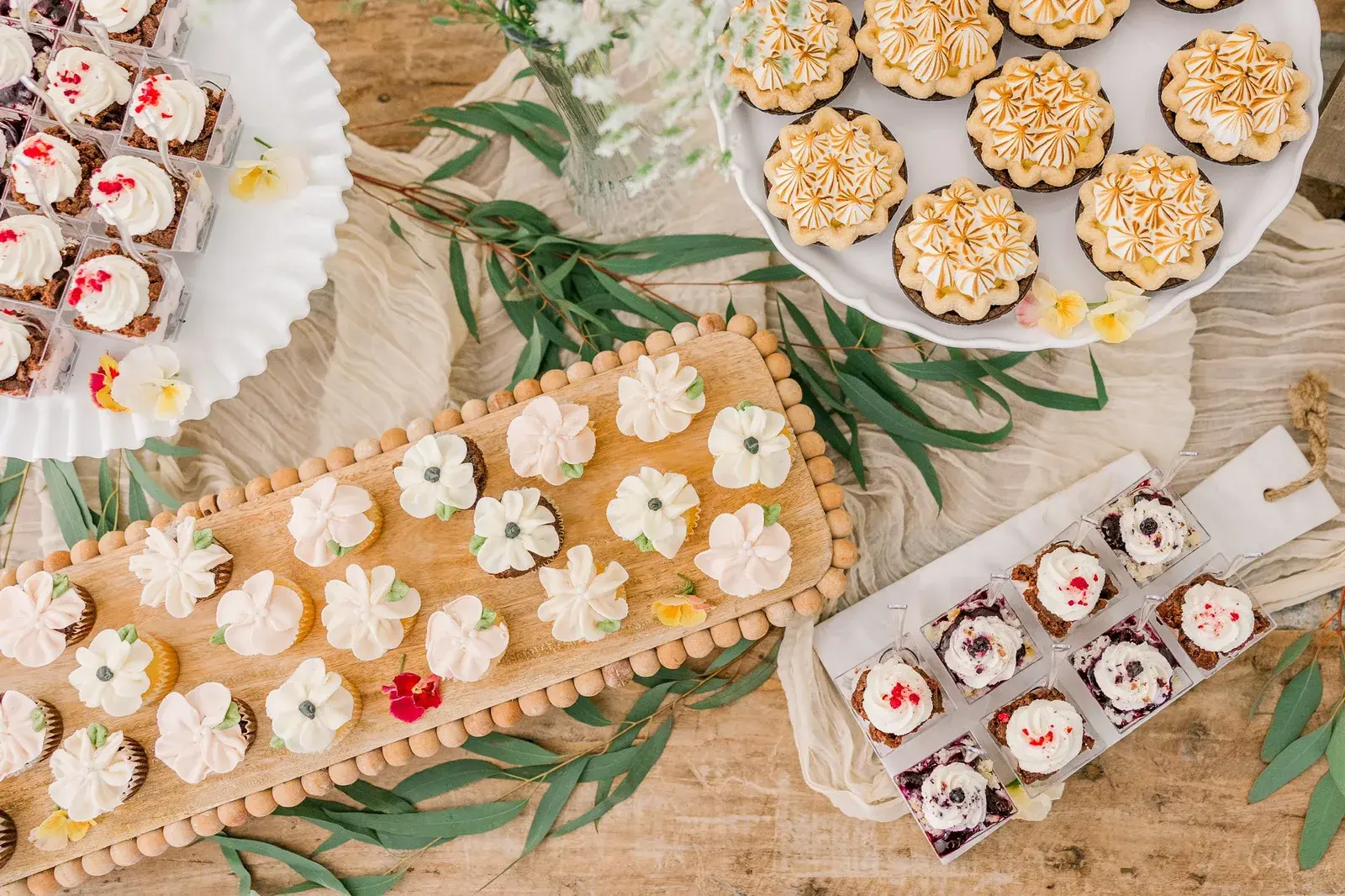 Mini cupcakes, meringue tarts and mini desserts arranged on wooden boards