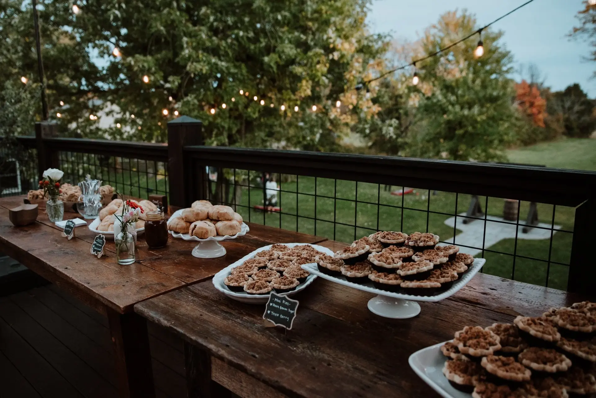 A wedding dessert table of cookies and mini pastries set out on a deck at dusk